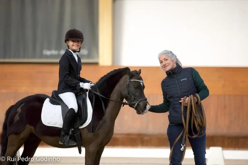 Uma jovem cavaleira e o seu pónei acompanhados pela sua treinadora Léa durante uma competição.